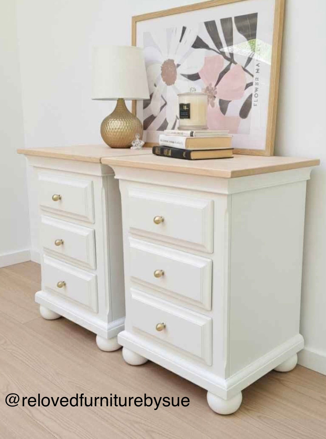 White bedside tables with wooden top and round solid brass knobs in a room with a lamp and artwork.