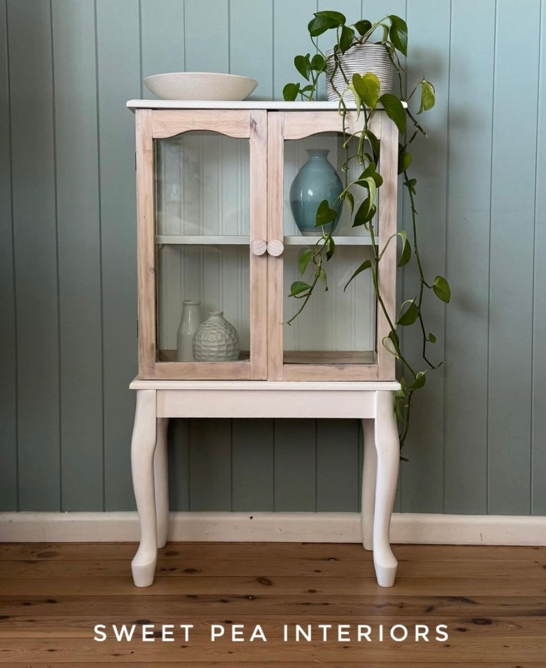 glass timber cabinet against green wall sanded back to raw timber with raw unfinished timber drawer knobs