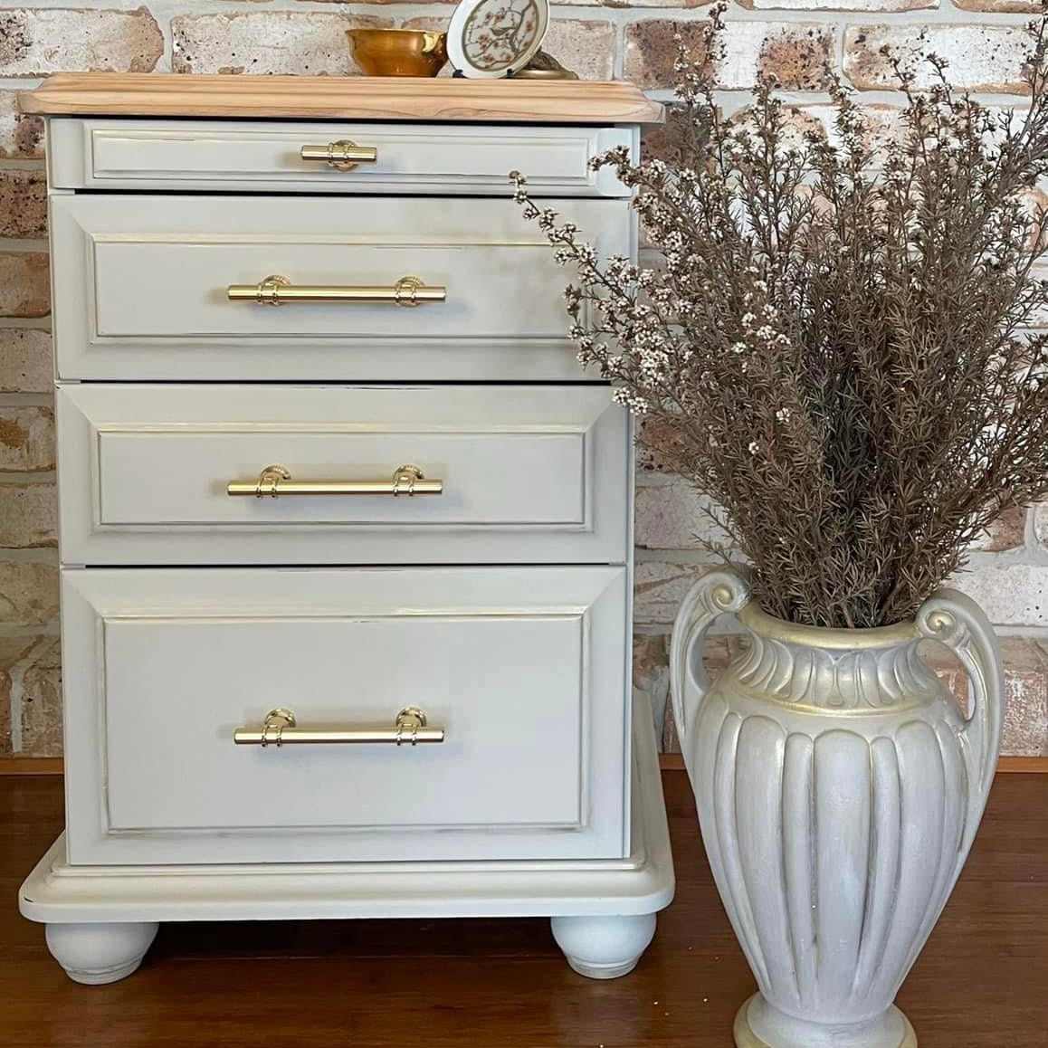 white painted bedside table upcyled with brick background wall and vase with gold drawer handles
