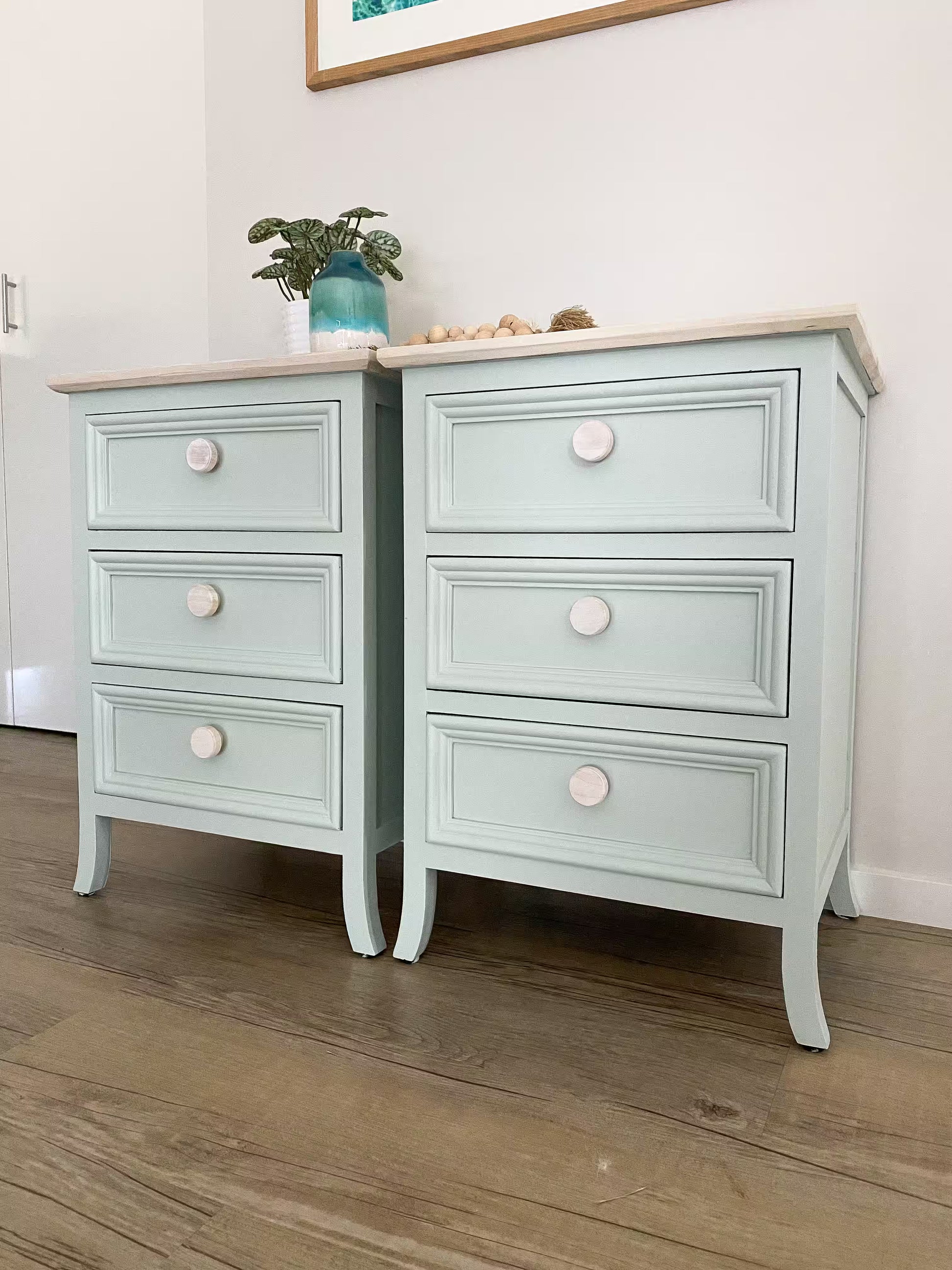 Light green bedside tables with white wooden drawer knobs on wooden floorboards