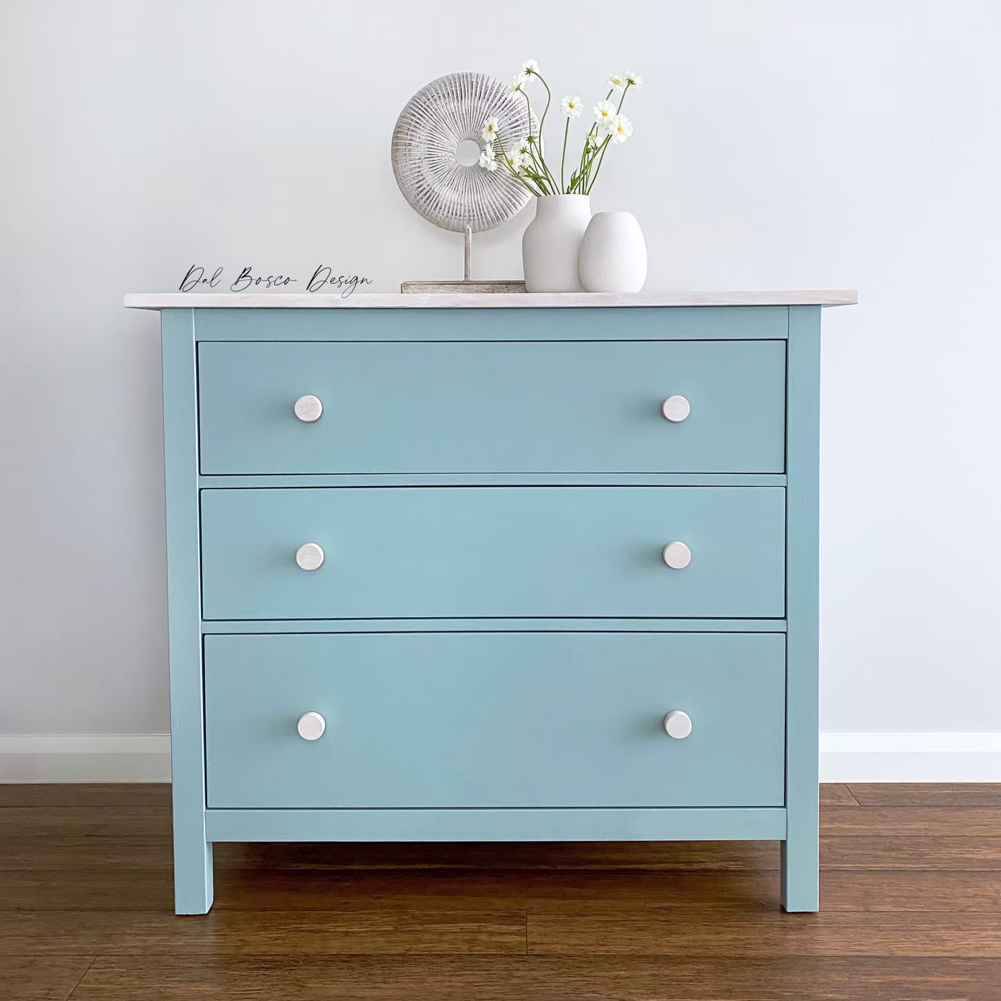 Light blue IKEA Hemnes dresser with white drawer knobs on a wooden floor and white wall.