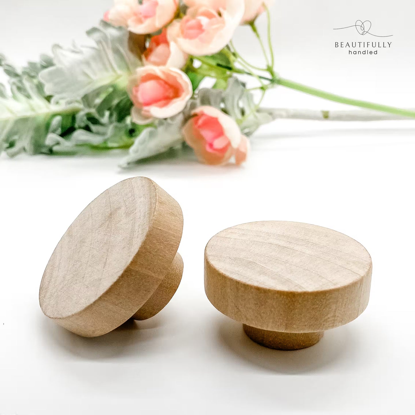 Two wooden knobs on a white surface with flowers in the background