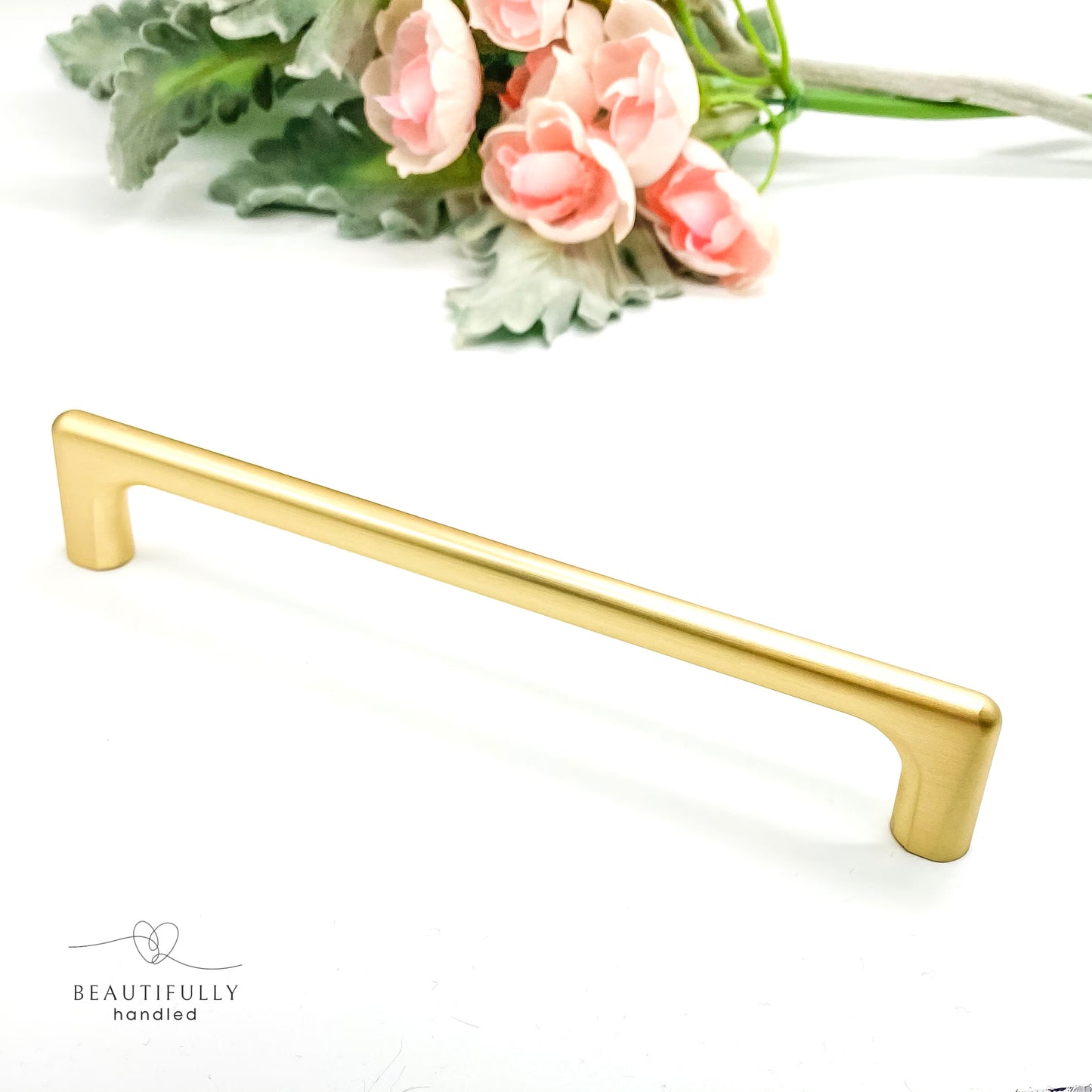Gold cabinet handle 160mm on a white background with pink flowers and green leaves.