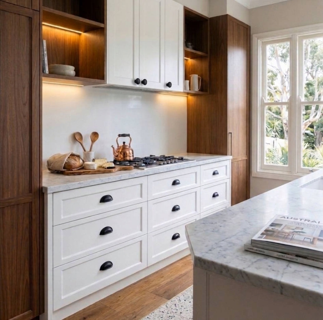 Luxury modern Hamptons kitchen renovation featuring white Shaker style cabinetry drawers with matte black cup pulls, white marble benchtops, warm walnut timber shelving, and matching matte black round knobs on overhead cupboards