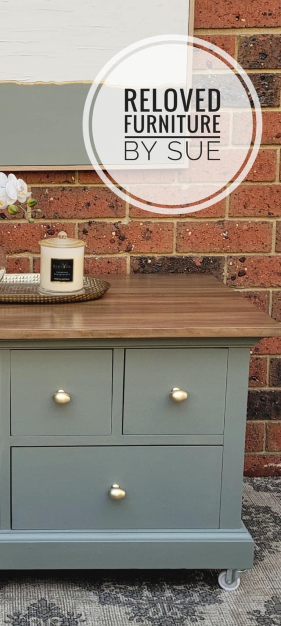 Reloved Furniture by Sue coffee table with a wooden top and gray base cabinet against a brick wall.