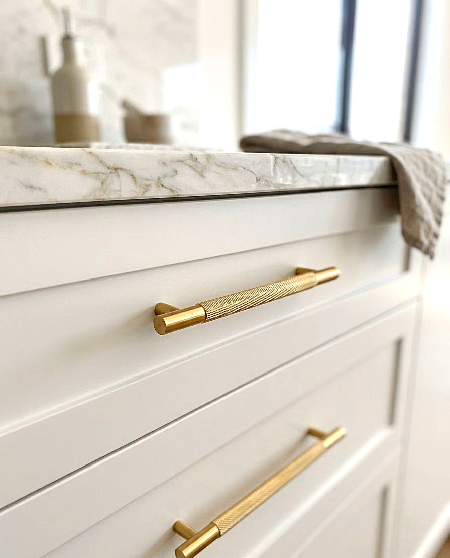 White bathroom shaker cabinet featuring knurled brass handles and a marble countertop