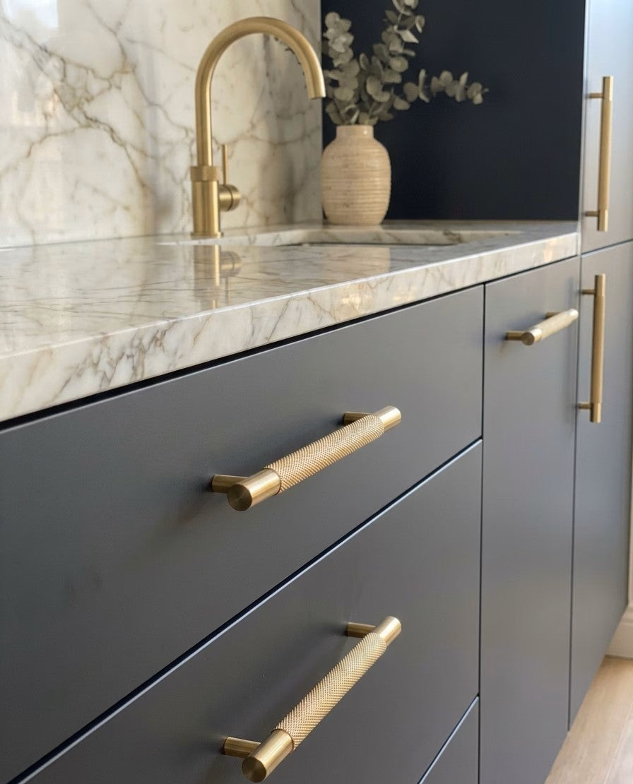 Modern kitchen with gray cabinets, knurled brass handles, and marble countertop also featuring brass tapware