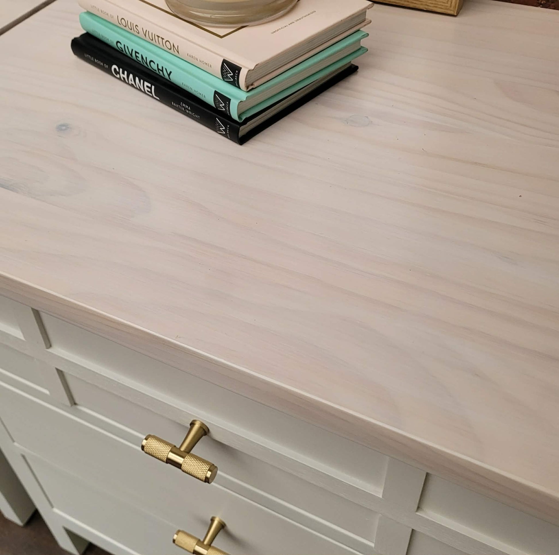 Close-up of a light wood dresser with brass knurled handles and books stacked on top.