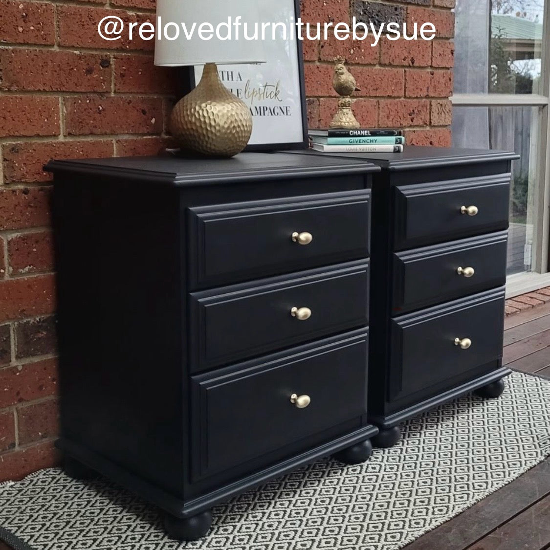 Side angle of black bedside tables with brushed gold knobs in egg shape in front of brick wall on rug