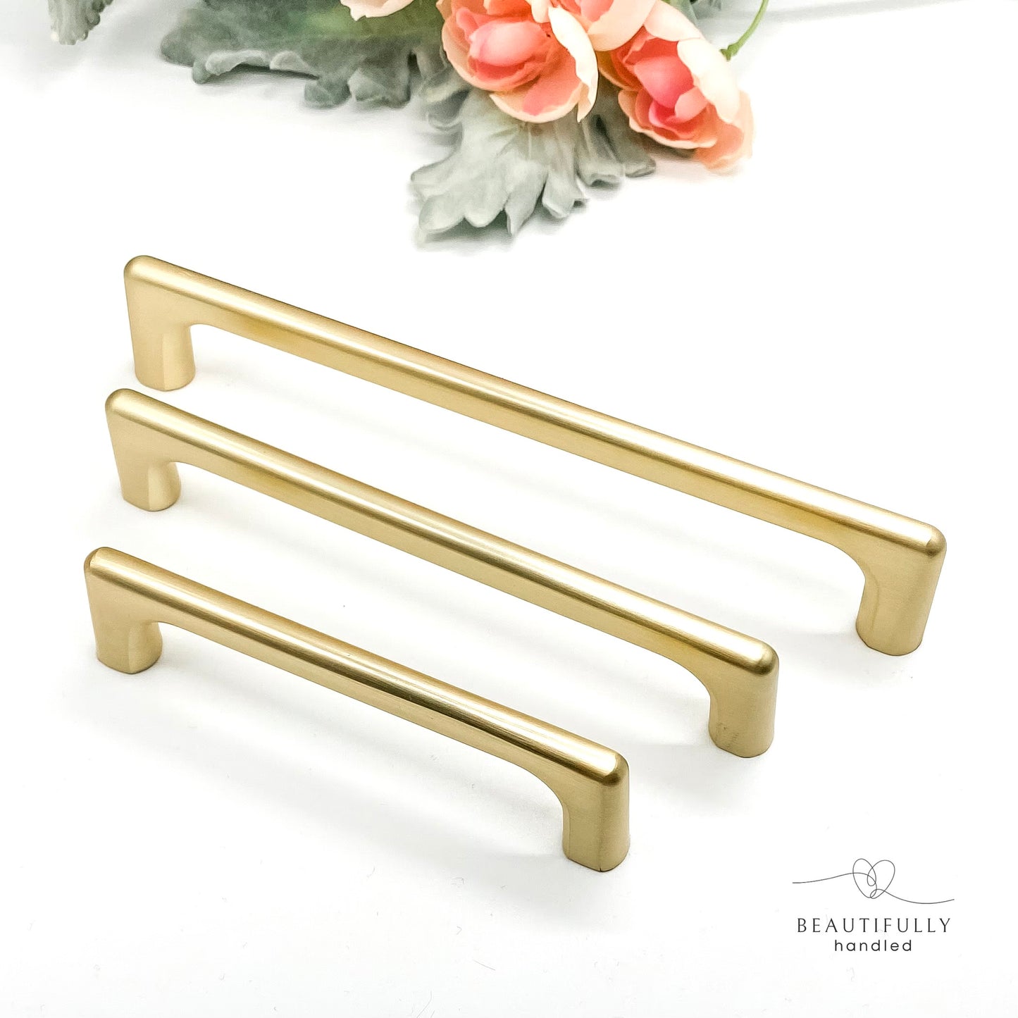 Side angle of three brushed gold handles on white background