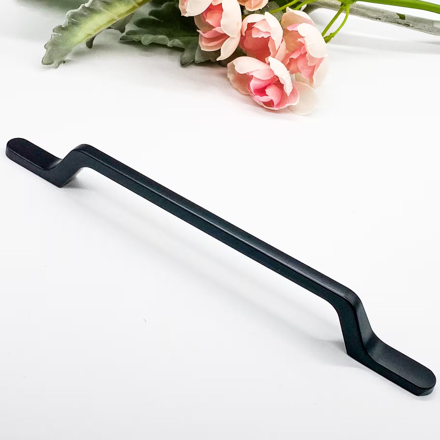 Black cabinet handle on a white background with pink flowers in the corner
