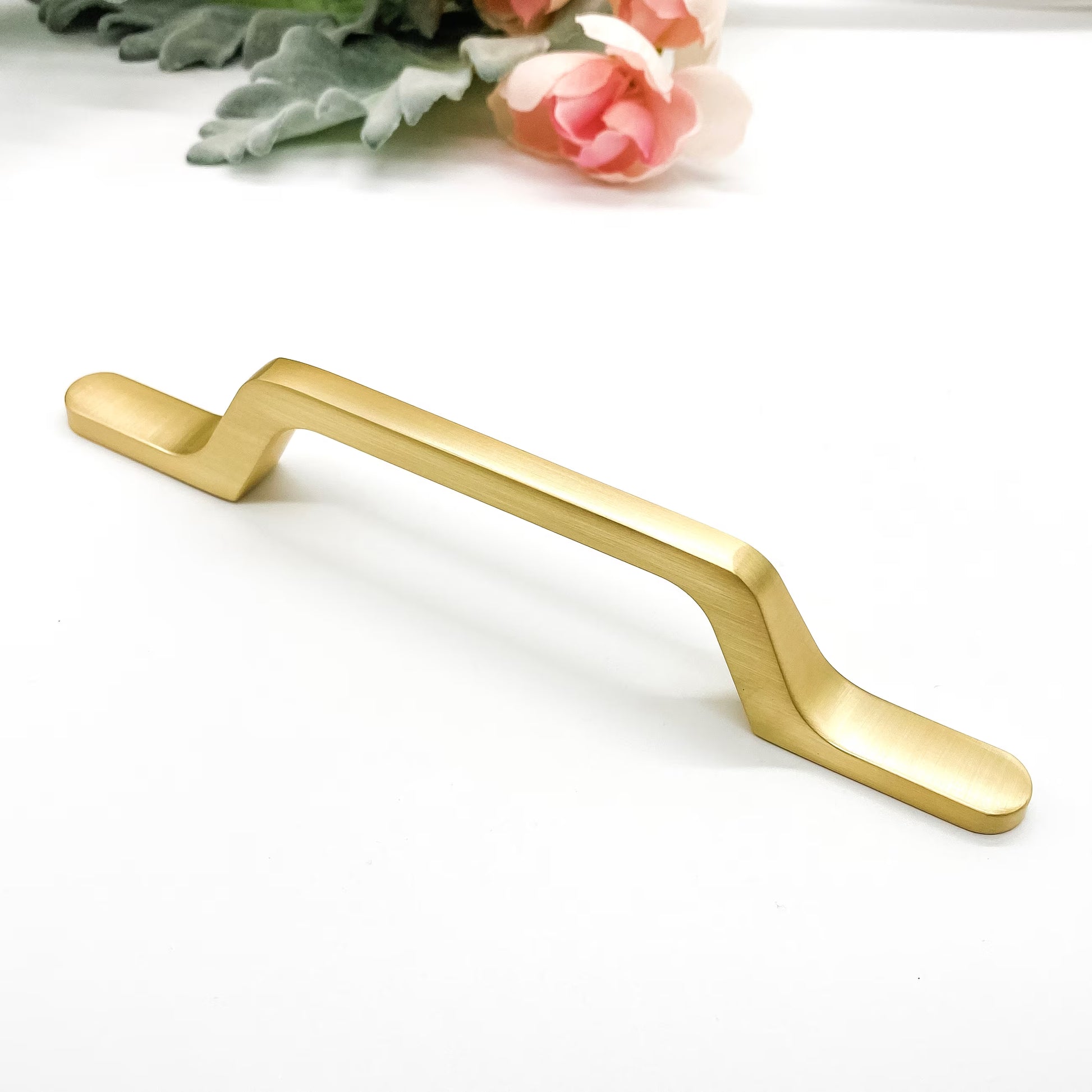 Gold cabinet handle on a white background with floral elements.