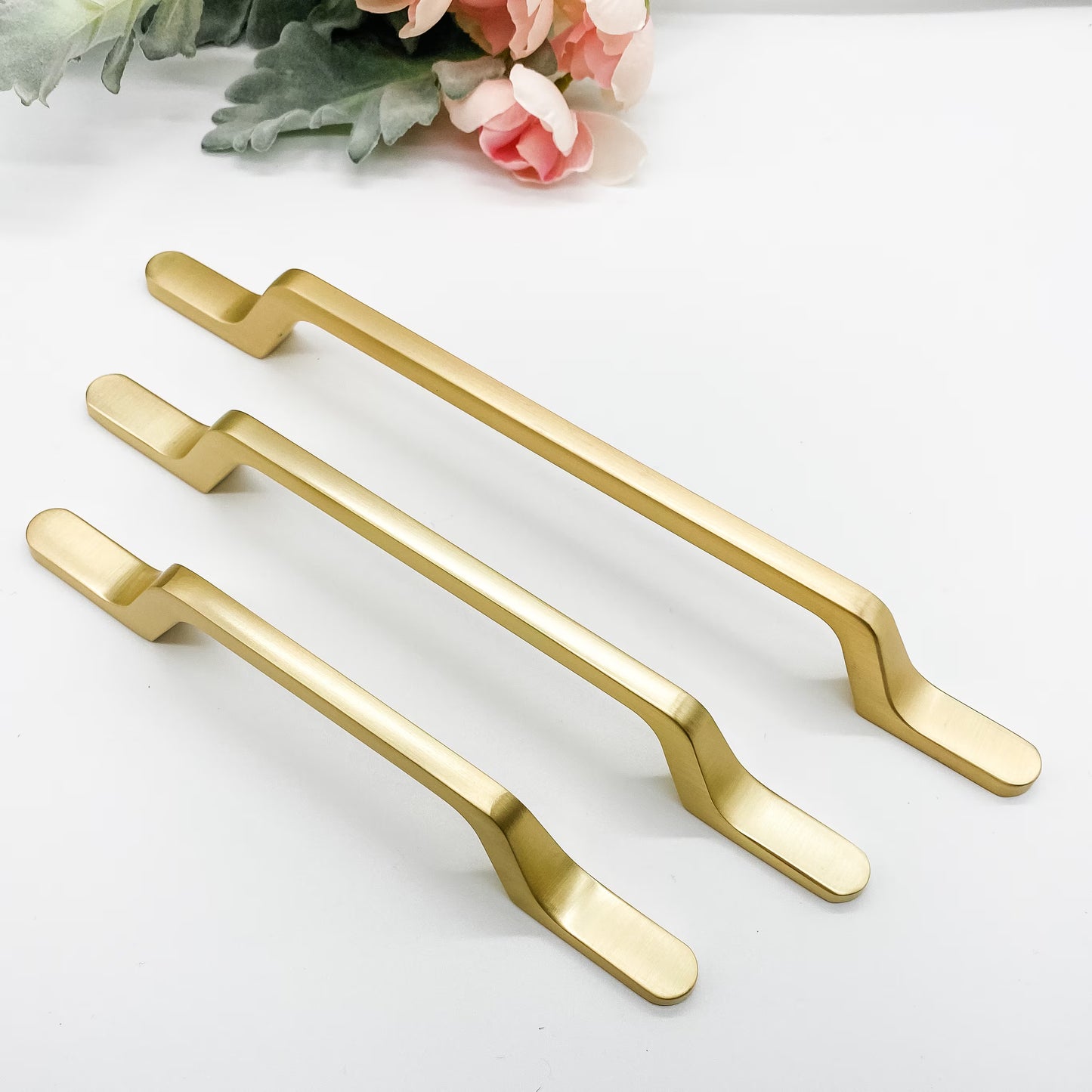 Three slimline gold cabinet handles on a white background with flowers.