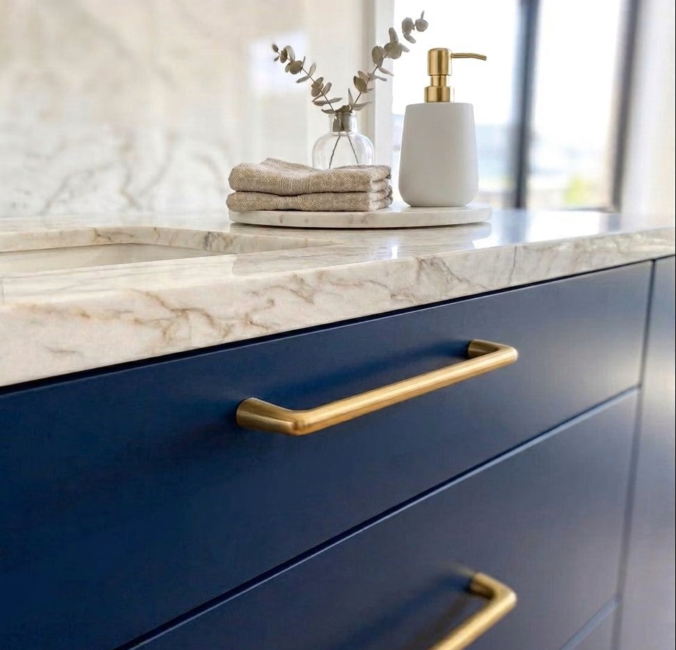 Bathroom vanity with blue cabinets, brushed gold square edged handles, and marble countertop.