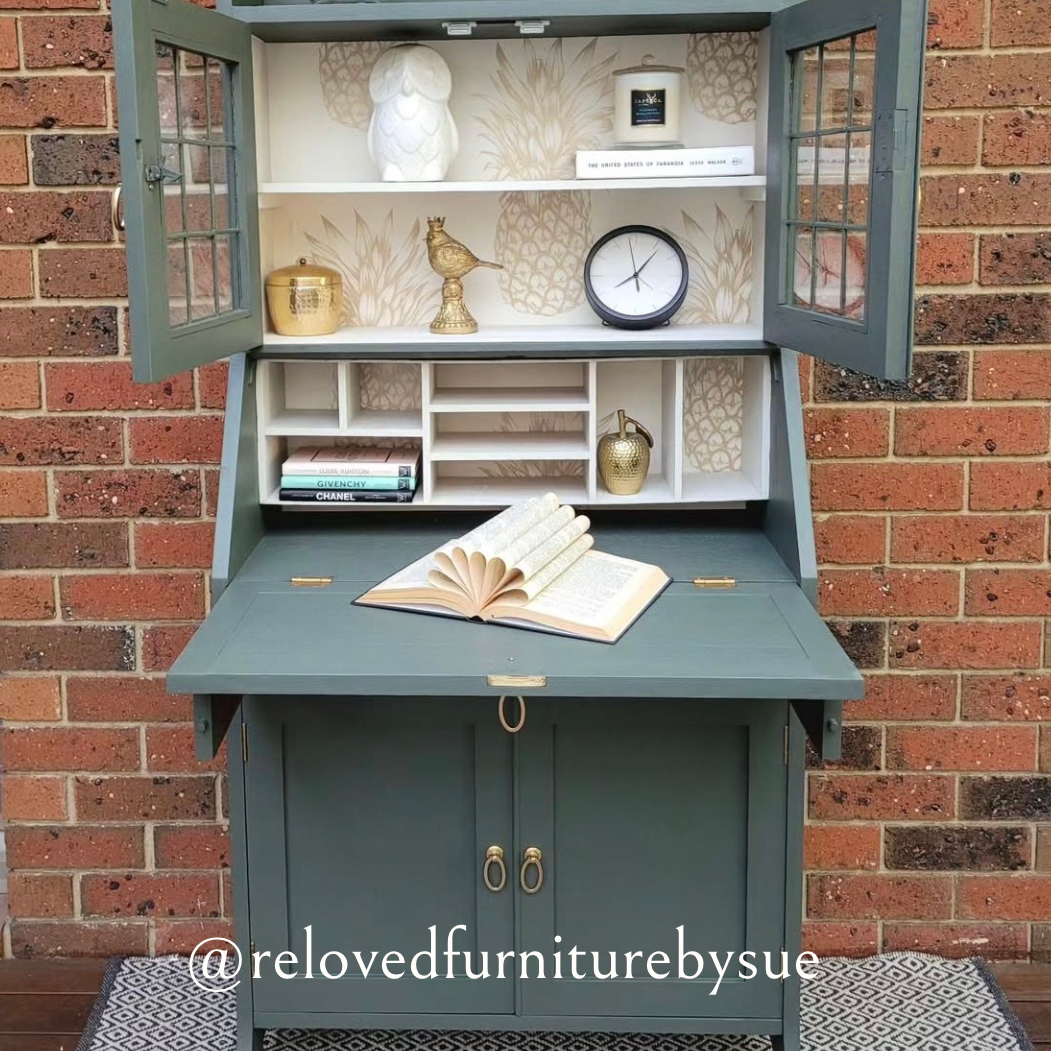 brushed gold oval shaped drop ring pull on sage coloured antique desk with brick wall behind