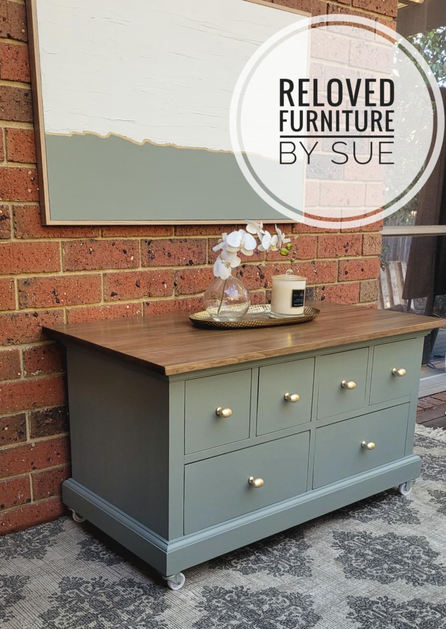 Large sage green coffee table with a wooden top featuring brushed gold drawer knobs cabinet against a brick wall - side angle.
