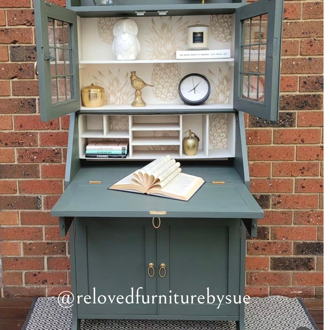 brushed gold oval shaped drop ring pull on sage coloured antique desk with brick wall behind
