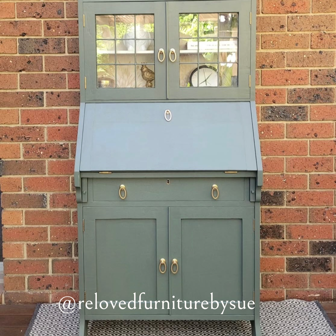brushed gold oval shaped drop ring pull on sage coloured antique desk with brick wall behind