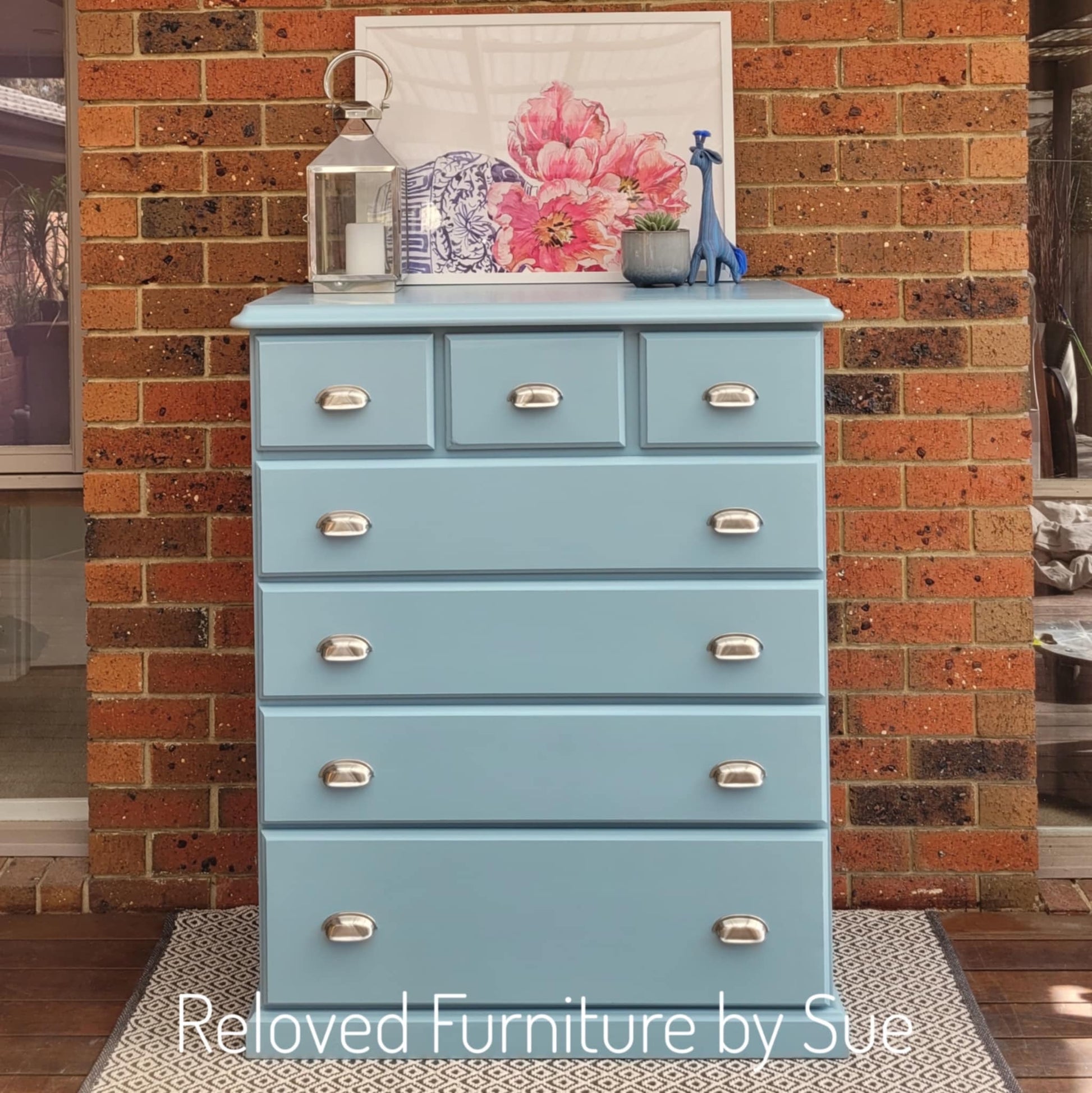 light blue chest of drawers with chrome cup pulls in front of red brick wall on patterned rug