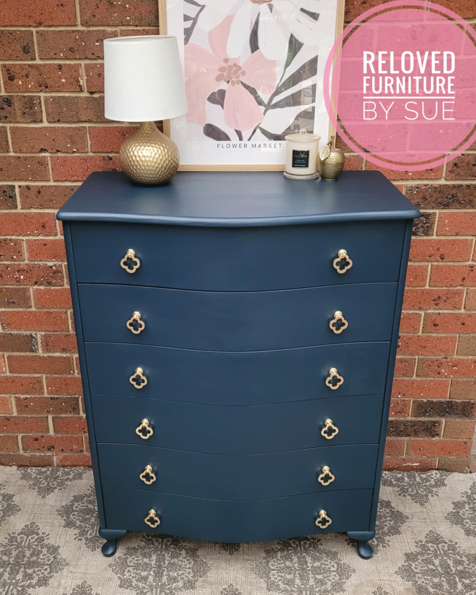 brushed gold clover leaf drawer handles displayed on nayy blue chest of drawers in front of brick wall and on rug