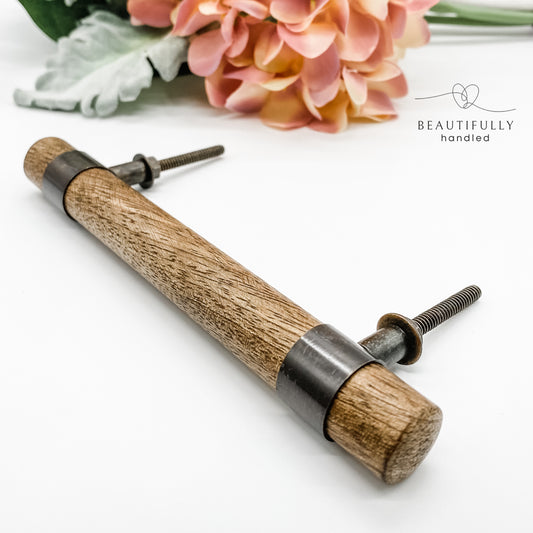 A hand-crafted wood and metal drawer handle with a contemporary design, displayed alongside floral decor.