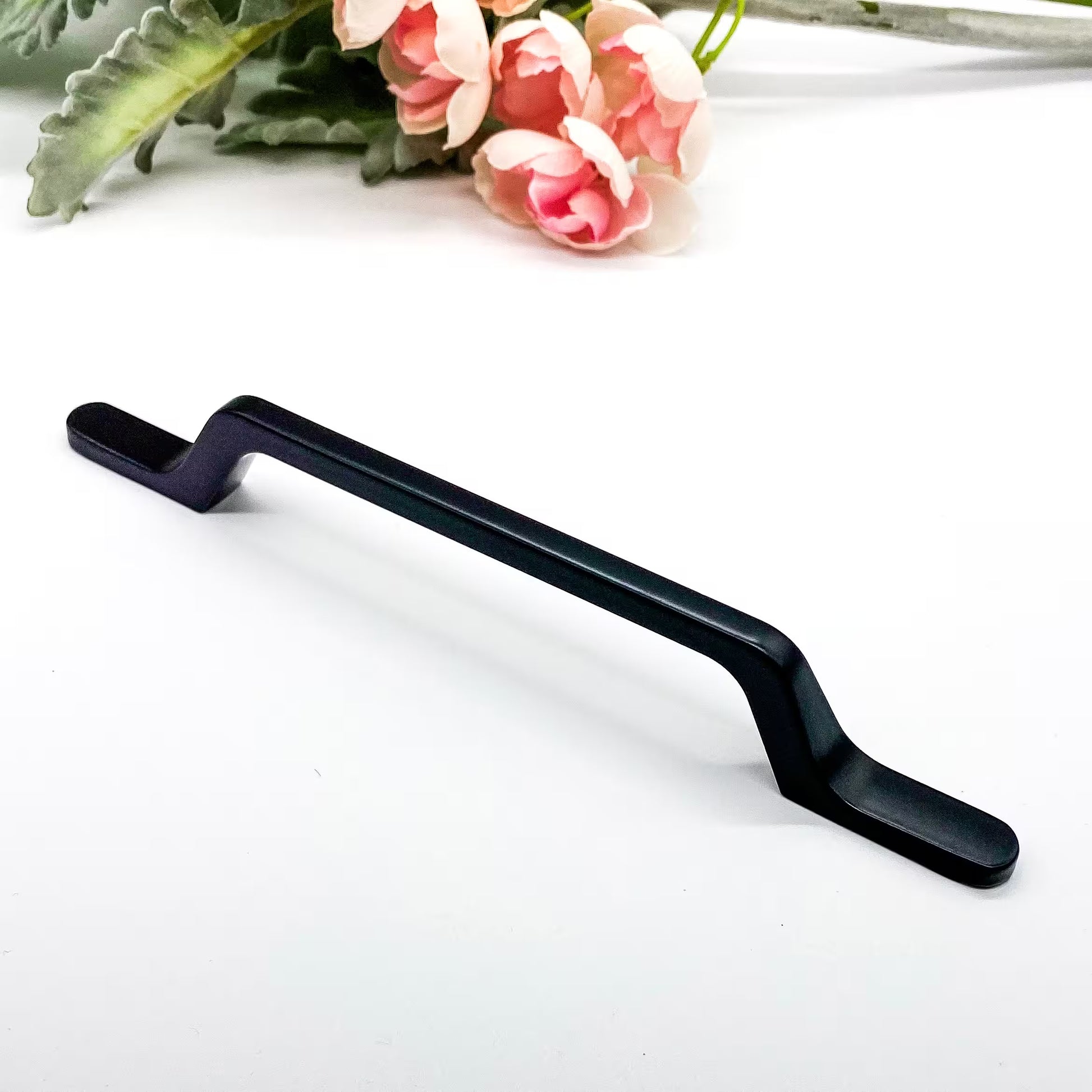 Black metal drawer handle on a white background with pink flowers and green leaves.