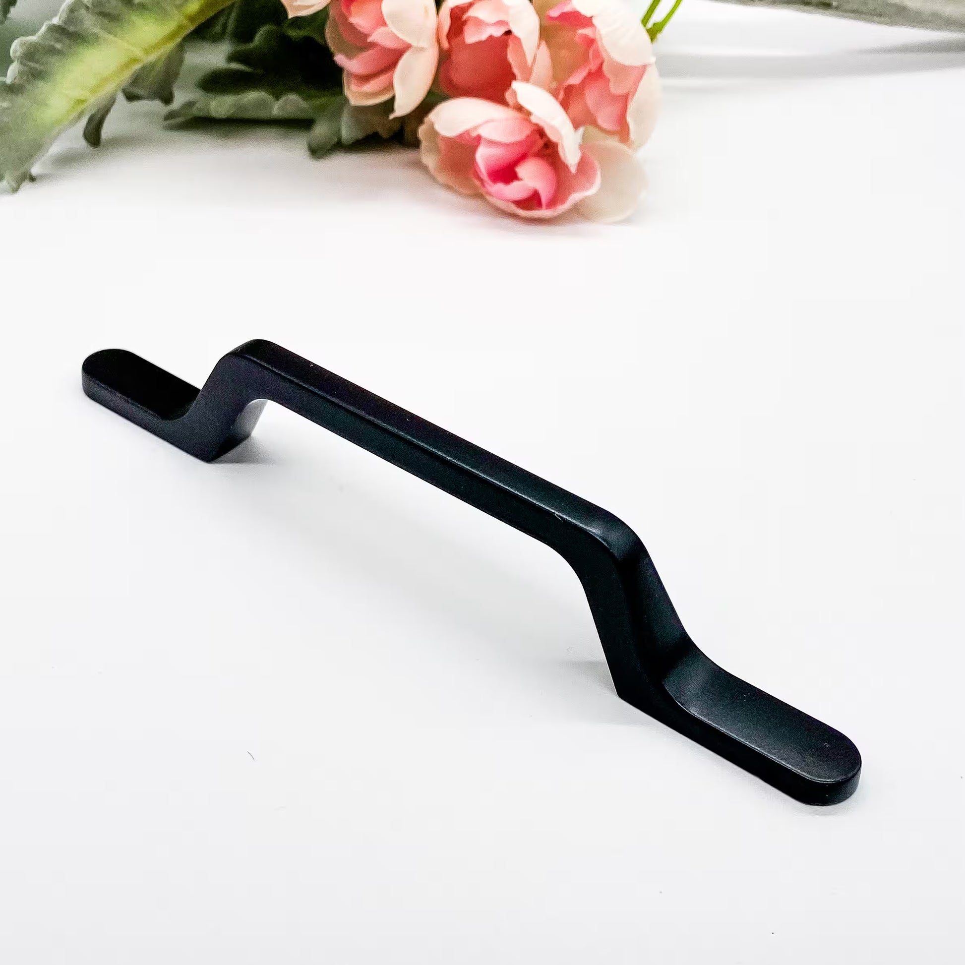 Black metal handle on a white surface with pink flowers and green leaves in the background