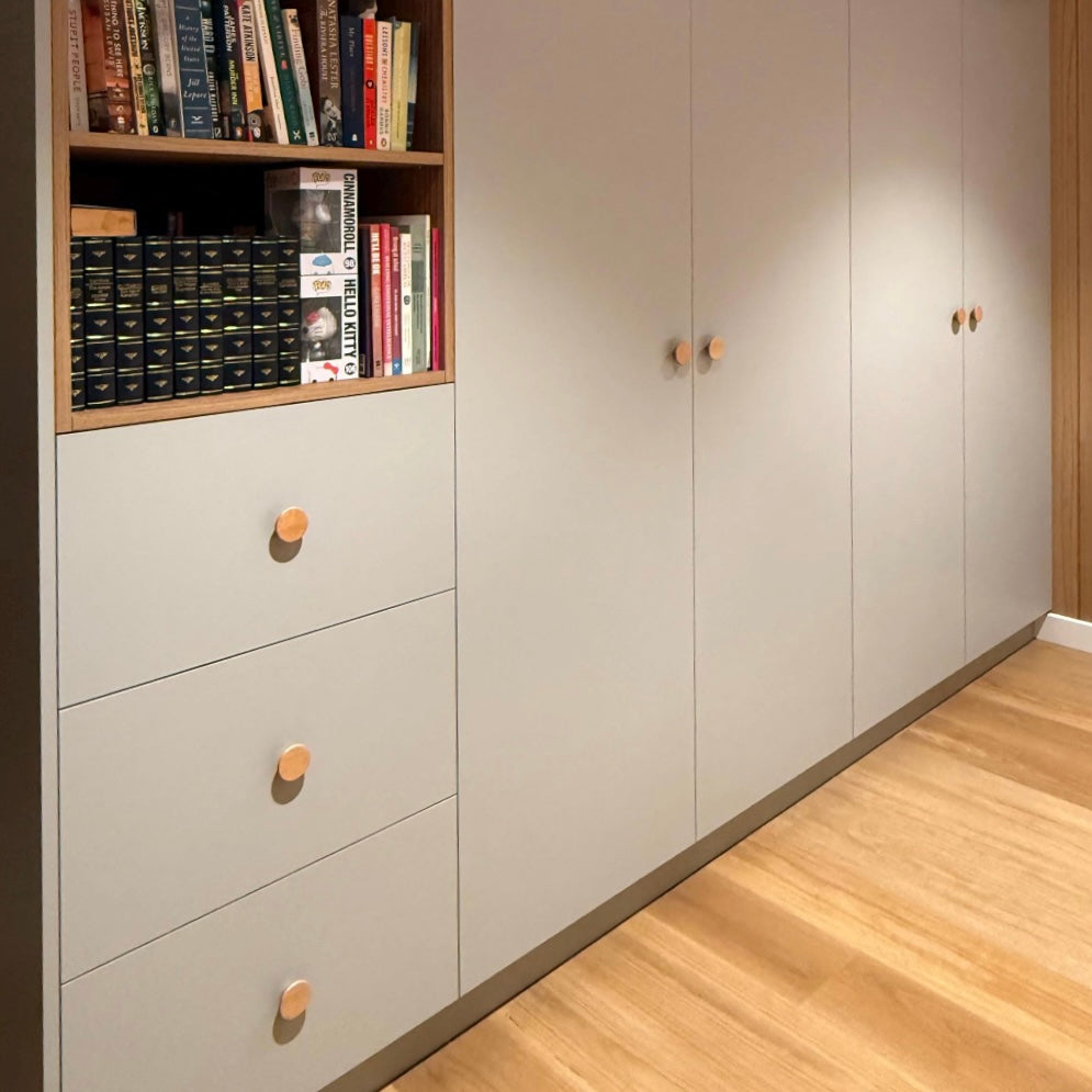 Light gray cabinets with wooden drawer knobs and a bookshelf against a neutral wall.