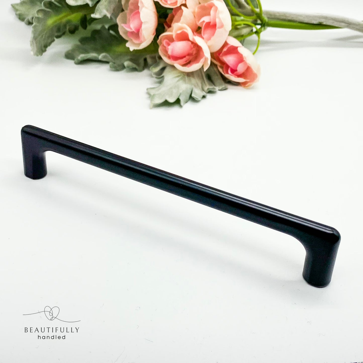 Black cabinet handle on a white background with pink flowers and green leaves.
